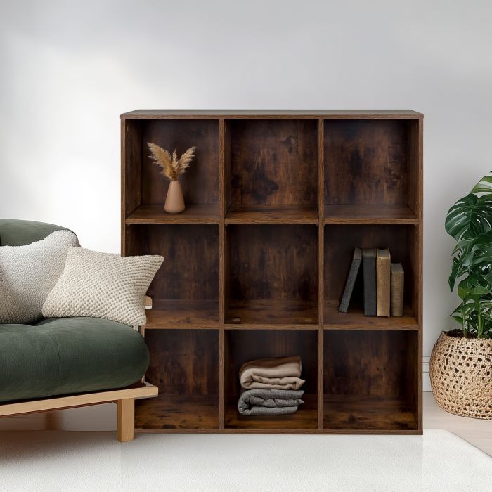 Tummanruskea tilanjakaja, jossa on koriste-esineitä, seisoo vihreän sohvan vieressä valkoisen seinän edessä.